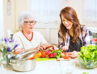 a caregiver assisting senior woman in preparing the vegetables