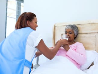 a caregiver assisting a senior woman in drinking one glass of milk