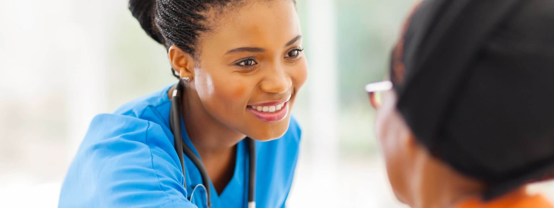 caring african medical nurse comforting senior patient in office