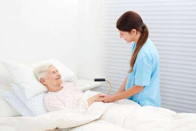 Senior lying in bed in hospice and talking to a caring caregiver