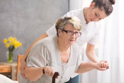 senior women with a walking stick and her professional carer helping her to stand up