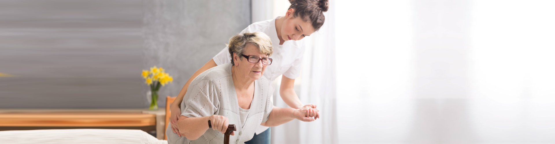 senior women with a walking stick and her professional carer helping her to stand up