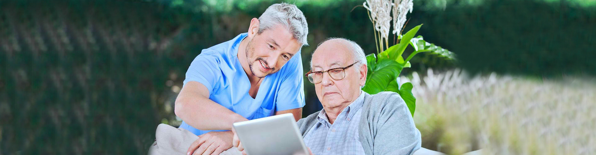 assisting senior men in using digital tablet at nursing home porch